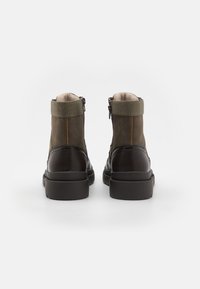 Botas de tobillo marrón y verde oliva con cuero texturizado, paneles de ante, cremalleras laterales y forro suave. Suelas de goma planas.