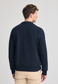 Felpa blu navy realizzata in morbido cotone, con collo a giro e polsini a coste. Presenta una vestibilità comoda e dettagli cuciti lungo l'orlo.