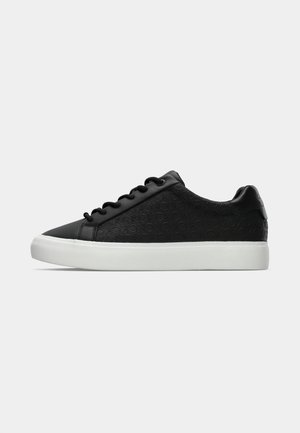 Svart sneaker med texturerad lädersida, vit gummisula och rund tå. Har platta snören och subtilt präglat logomönster.