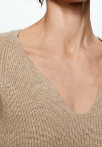 Beige gestrickter Pullover mit tiefem V-Ausschnitt, gerippter Textur und tailliertem Design, das aus einem weichen und leichten Material besteht.