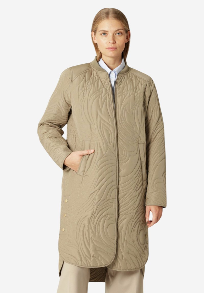 Abrigo acolchado beige con cuello alto, dos bolsillos laterales y patrones de costura decorativos. Acabados de botones en el dobladillo.