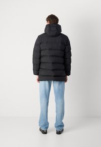 Zwarte pufferjack met een capuchon, met horizontaal gestikte delen, een ontspannen pasvorm en een gladde textuur. Draag het met lichtblauwe jeans.