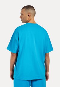 Camiseta oversized turquesa de manga corta, con cuello redondo y tejido suave. Presenta un corte relajado y un diseño minimalista.