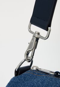 Sangle en cuir bleu foncé avec quincaillerie en métal argenté, dotée d'un connecteur à crochet snap, de coutures détaillées et d'une texture en denim sur le sac.