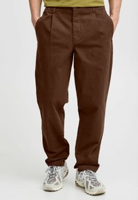 Braune, lässig geschnittene Hose mit Falten, aus Baumwolle. Verfügt über Seitentaschen und einen Knopfverschluss am Bund.