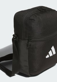 Černá látková taška přes rameno se zipovým uzávěrem, obsahující hladký povrch a výrazné bílé logo na jedné straně. Součástí je nastavitelný popruh.