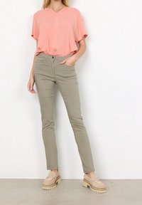 Blusa corta a maniche corte color pesco con scollo a V abbinata a pantaloni aderenti verde oliva. Mocassini beige con suola spessa offrono un aspetto bilanciato.