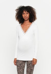 Top bianco a maniche lunghe con scollo a V incrociato e bordo in pizzo, indossato con leggings a fantasia con stampa leopardata.