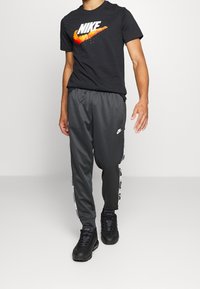 Svart Nike-t-shirt med en färgglad logotyp, ihop med grå träningsbyxor med sidodesign och svarta träningsskor.