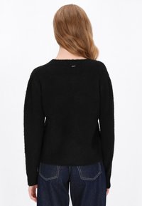 Sort, textured sweater med en afslappet pasform, lange ærmer og en rund halsudskæring. Har et lille, sølvfarvet logo-tags på ryggen.