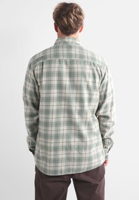 Chemise flanelle à carreaux verts avec des accents blancs et bleus, dotée d'un design à boutons et de manches longues, présentée de dos.