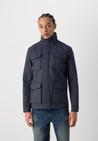 Jacket bleu marin cu guler înalt, patru buzunare frontale și buzunare laterale cu fermoar. Fabricat dintr-un material texturat, cu închidere cu fermoar în față.