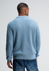 Hellblauer, gerippter Strickpullover mit Kragen und langen Ärmeln, kombiniert mit lässigen blauen Jeans. Rückansicht.