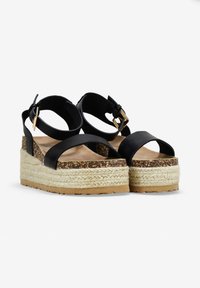 Sandalias de plataforma negras con una suela intermedia de yute trenzado, con dos correas frontales y una correa para el tobillo ajustable con una hebilla en tono dorado.