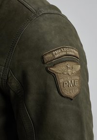Chaqueta de cuero verde con un acabado texturizado, detalles cosidos y un prominente parche de tela marrón con el logo de PME y la marca American Classic.