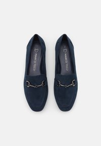 Paire de mocassins en daim bleu marine avec détail mors argenté et marquage "Marco Tozzi" à l'intérieur, vus de dessus sur un fond blanc.