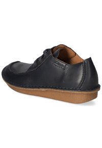 Zapato de cuero negro con puntera redondeada, costuras decorativas, dos ojetes para los cordones y una suela de goma marrón. Diseño sencillo y funcional.
