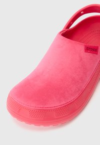 Helle pinke Crocs-Clogs mit weichem, strukturiertem Obermaterial und ventiliertem Riemen, seitliche Ansicht, die vordere und seitliche Details auf weißem Hintergrund zeigt.
