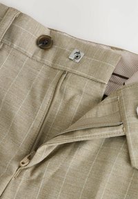 Pantaloni in lino beige con motivo a righe, zip frontale e chiusura con bottone, accentati da dettagli in metallo argentato. L'interno presenta un rivestimento a righe.
