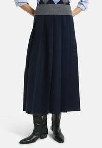 Diepblauwe geplooide rok van gladde stof met een grijze elastische tailleband, gecombineerd met zwarte leren enkellaarsjes met een rits.