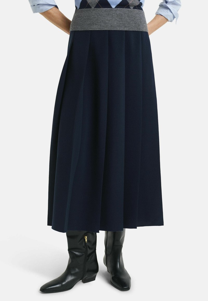 Diepblauwe geplooide rok van gladde stof met een grijze elastische tailleband, gecombineerd met zwarte leren enkellaarsjes met een rits.