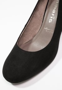 Chaussure plate femme en daim noir à bout rond, intérieur beige matelassé et nom de marque imprimé à l'intérieur.