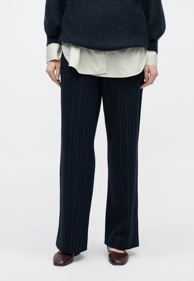 Marineblå bukser med nålestriber og et lige ben design, kombineret med en lys, lagdelt skjorte. Har en glat tekstur og skræddersyet pasform.