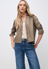 Hellbraunes Hemd mit Knopfleiste und hochgekrempelten Ärmeln, kombiniert mit hoch taillierten blauen Jeans im weit geschnittenen Stil. Schlichtes Design und glatte Textur.
