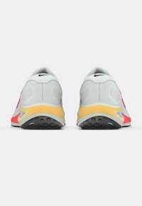 Ζευγάρι λευκά και κόκκινα αθλητικά παπούτσια με κίτρινες μεσαίες σόλες, εμφανιζόμενα από πίσω σε λευκό φόντο.