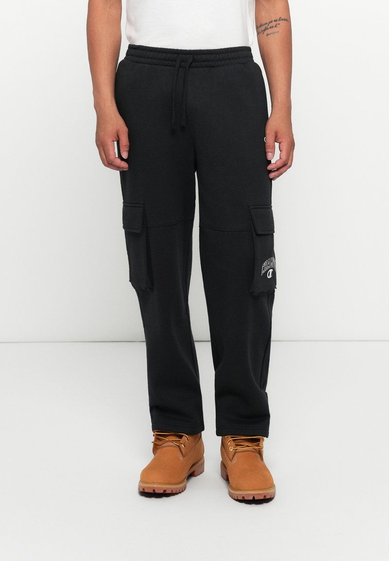 Sorte cargo-joggers med elastisk talje, sidelommer og broderet logo. Kombineret med mellembrune støvler og en hvid t-shirt.