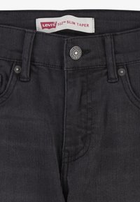 Jeans Levi's 512 Slim Taper de mezclilla oscura con un botón plateado, costuras en contraste y una etiqueta en la cintura. Textura suave.