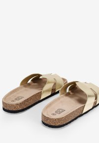 Sandalias de imitación de cuero dorado con dos correas anchas, una plantilla de corcho y una suela de goma negra texturizada. La plantilla es de color beige claro.