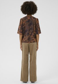 Haut plissé tie-dye marron à manches courtes, associé à un pantalon en velours côtelé à jambes larges dans un ton beige atténué. Vue arrière montrant les détails de conception.