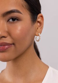 Perlen-Hoops mit kreisförmigem Design, ausgestattet mit mehreren kleinen weißen Perlen und einem silberfarbenen Metallverschluss. Glatte Textur und elegantes Design.