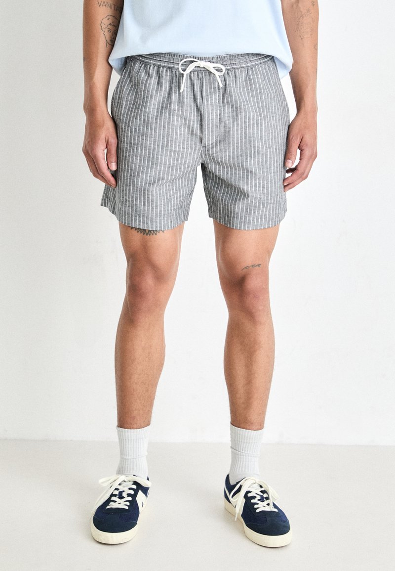 Striped gray swim shorts with an elastic waistband, white drawstring, and frayed hem; paired with navy sneakers and white ankle socks.
