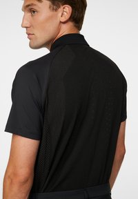 Svart kortärmad polo t-shirt med en texturerad baksidedesign med vertikala linjer, tillverkad av ett lätt och andningsbart material.