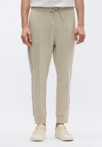 Vaaleanbeiget collegehousut, joissa on kiristysnyöri vyötäröllä, kapea istuvuus, resorit lahkeensuissa ja hienovaraisesti teksturoitu kangas. Yhdistetty vaaleisiin tennareihin.