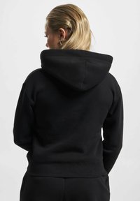 Černá mikina s kapucí, velkou kapucí, žebrovanými manžetami a lemem, vyrobená z měkké tkaniny. Design je jednoduchý a dobře padne v pase.