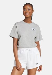 Grå t-shirt med kort ärm har rund halsringning och en cirkulär logga på bröstet. Matchas med vita shorts med elastiskt midjeband och ficka.
