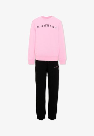 Sweat-shirt rose avec le texte "John Richmond" associé à un pantalon de jogging noir comportant un petit texte assorti sur la zone de la poche.