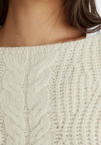 Suéter de punto trenzado crema con patrones en relieve, superficie texturizada, escote amplio y material de mezcla de lana suave y esponjoso.