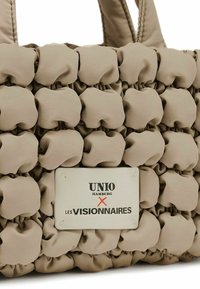 Borsa a tote beige con una superficie tessurizzata e imbottita. Presenta un'etichetta rettangolare con il testo "UNIO HAMBURG X LES VISIONNAIRES". Doppi manici.