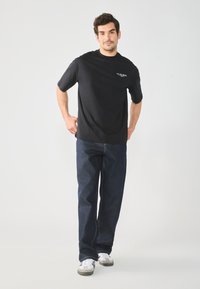 Black cotton t-shirt with short sleeves and crew neck, paired with dark blue denim jeans featuring a center front seam and casual sneakers.