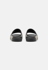 Black slide sandals with open back and round toe. Smooth rubber-like material, featuring subtle textured stripes and gold accents on the sides.