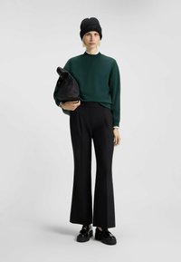 Felpa verde, pantaloni neri a vita alta, berretto nero e scarpe nere lucide. Colori solidi con vestibilità rilassata; texture lisce.