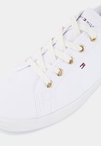 Białe płócienne sneakersy z złotymi oczkami, beżowymi sznurówkami i fakturowaną gumową podeszwą. Posiada mały detal z logo po boku.
