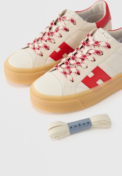 Λευκά αθλητικά παπούτσια με κόκκινες λεπτομέρειες, που διαθέτουν υφή στη σόλα, κορδόνια με σχέδιο και εμφανές λογότυπο. Περιλαμβάνεται ένα επιπλέον μπεζ κορδόνι.