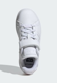 Sneaker blanche avec une tige en cuir lisse, doublure en mesh texturé, lacets plats et une sangle. Présente un logo "Star Wars" à l'intérieur.