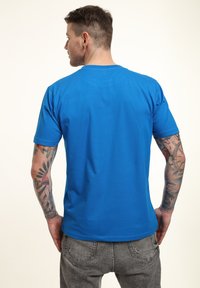 Modrá krátkým rukávem tričko s hladkou texturou, kulatým výstřihem a běžným střihem, spojené se šedými roztrhanými džíny.