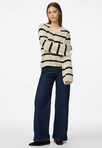 Gebreide crèmekleurige trui met zwarte strepen, ruime pasvorm en geribbelde textuur, gecombineerd met hoge, donkerblauwe wijde jeans.